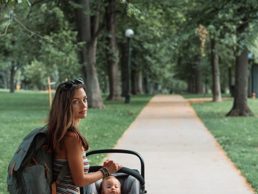 Woman pushing stroller along a tree-lined path in a Denver park